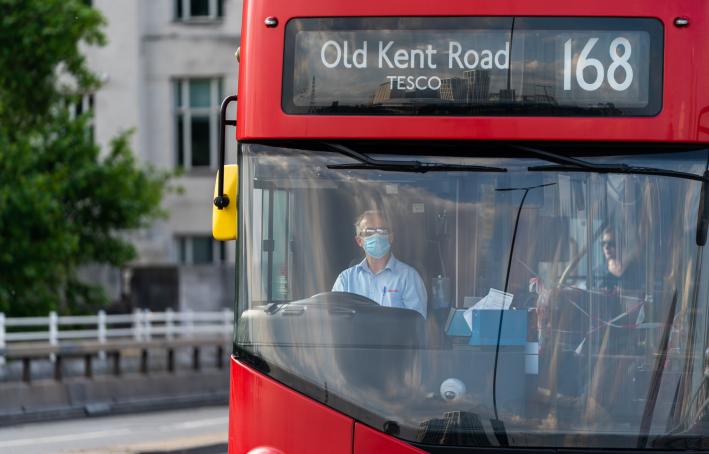 Driver of a double decker red London Bus driving with a face mask on