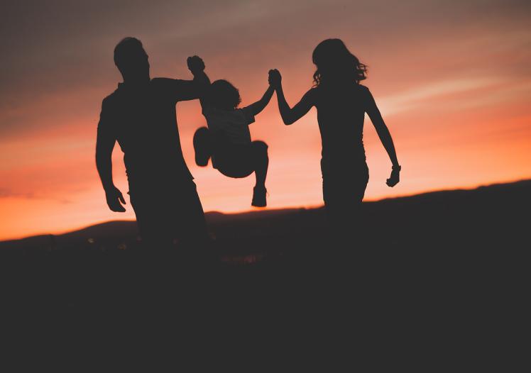 Mother and Father swinging son up in the air at sunset 