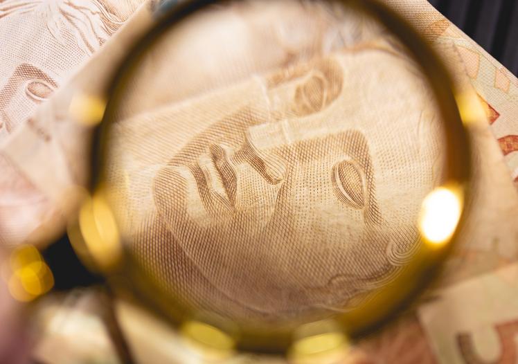 Brazilian Real banknotes and a golden magnifying glass