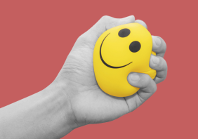 Hand squeezing smiling face yellow stress ball,
