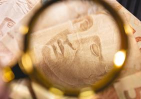 Brazilian Real banknotes and a golden magnifying glass