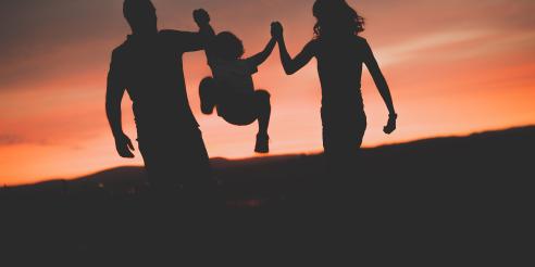 Mother and Father swinging son up in the air at sunset 