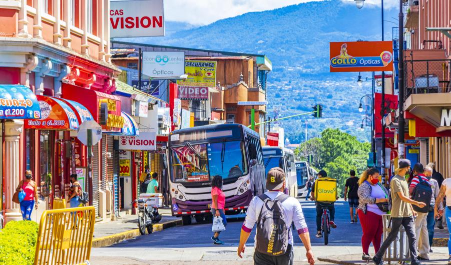 Colorful bus busses in busy traffic and cityscape with stores people and cars in San José Costa Rica