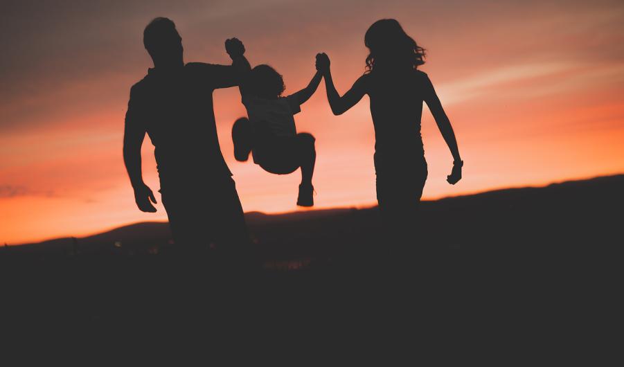 Mother and Father swinging son up in the air at sunset 