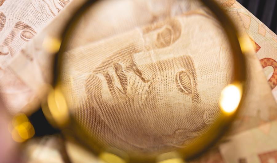 Brazilian Real banknotes and a golden magnifying glass