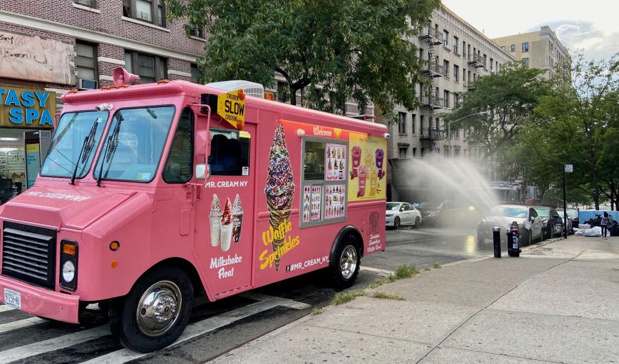 Pink ice cream truck parked on a street in front of an open hydrant on a summer evening in New York City